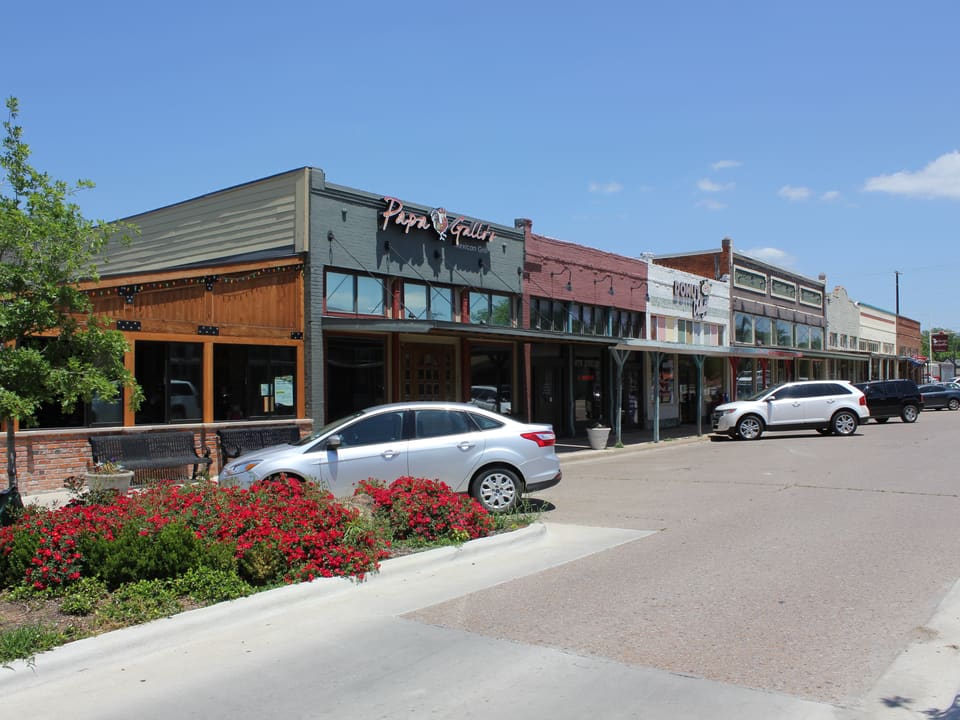 Brick storefronts and a flower-lined median along the downtown square in Celina, Texas.