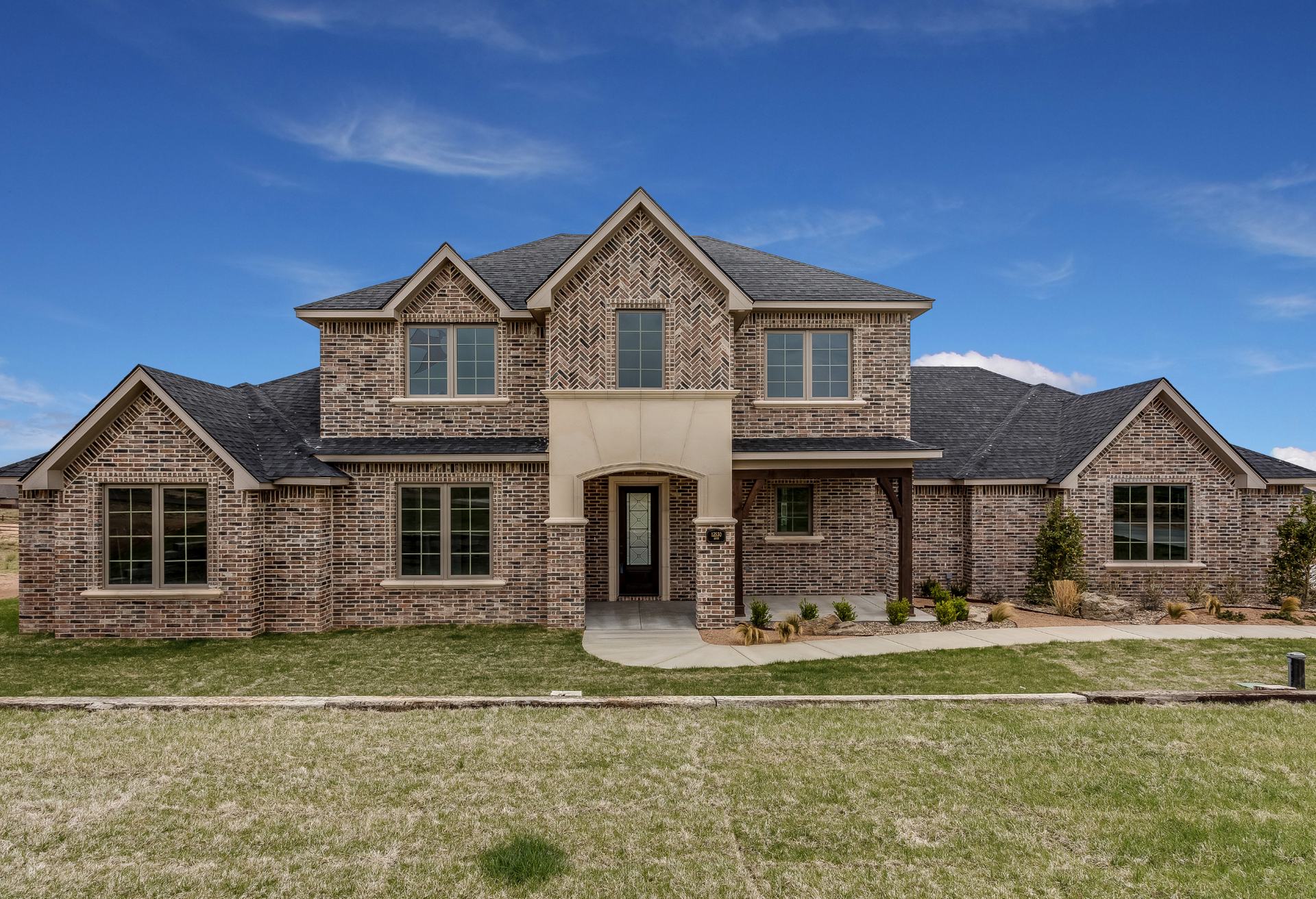 A large two-story North Texas brick home with gabled rooflines and a manicured front lawn under a clear blue sky.