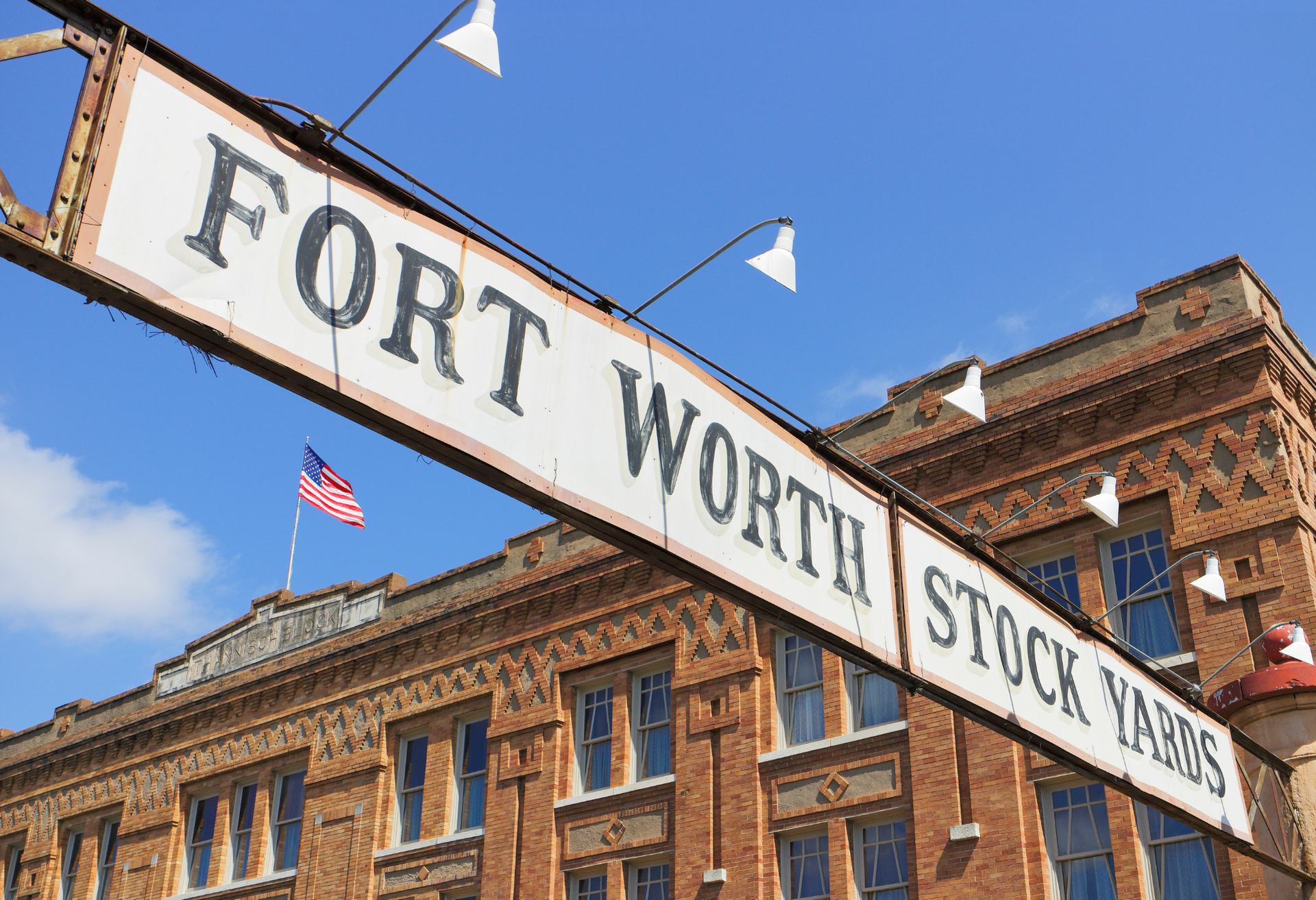 The historic Fort Worth Stockyards sign spanning a vintage brick building facade beneath a blue sky.