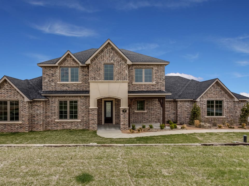 A two-story brick home with a manicured lawn and covered entry under a clear blue sky, representative of homes in the area.