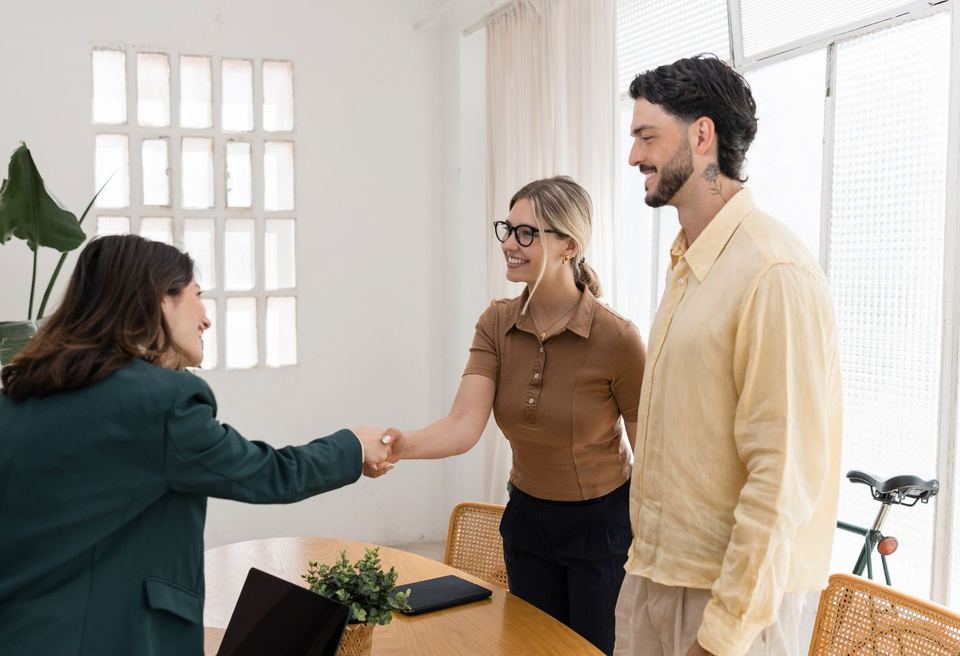 A real estate agent shaking hands with a happy couple in a bright room after closing on their home.